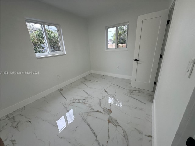 empty room featuring marble finish floor, plenty of natural light, and baseboards