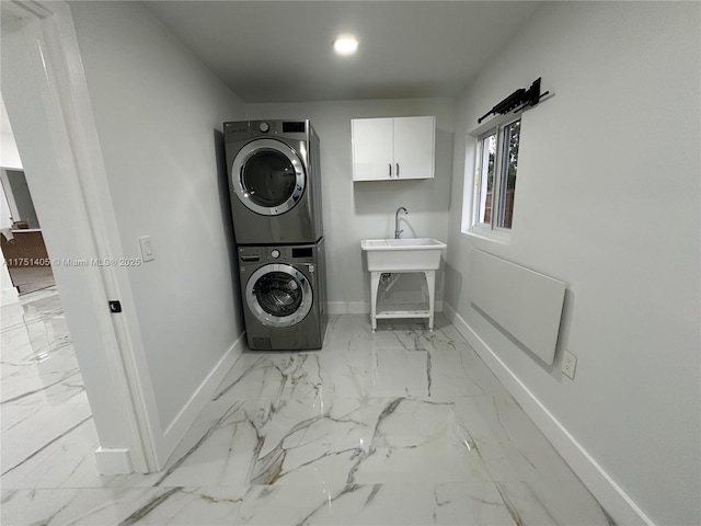 washroom featuring a sink, baseboards, marble finish floor, cabinet space, and stacked washer and clothes dryer