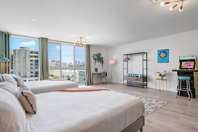 bedroom featuring a chandelier, a city view, visible vents, light wood-type flooring, and floor to ceiling windows