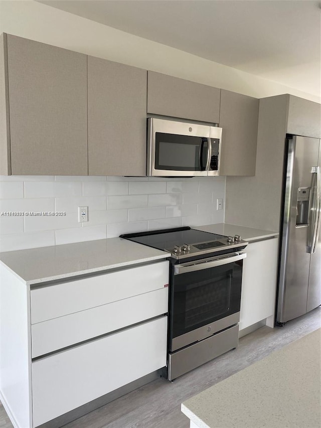 kitchen featuring stainless steel appliances, light wood-style floors, light countertops, gray cabinets, and tasteful backsplash