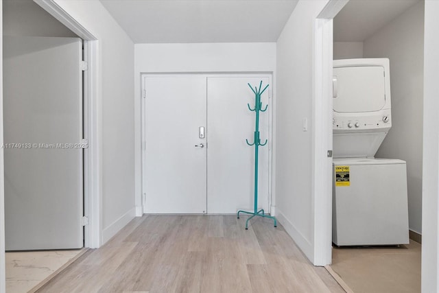 laundry room with stacked washer / drying machine, laundry area, baseboards, and light wood finished floors