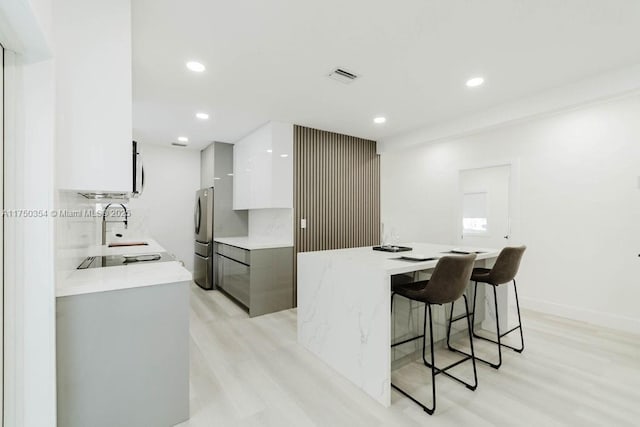 kitchen with light wood-style flooring, visible vents, a kitchen breakfast bar, white cabinetry, and modern cabinets