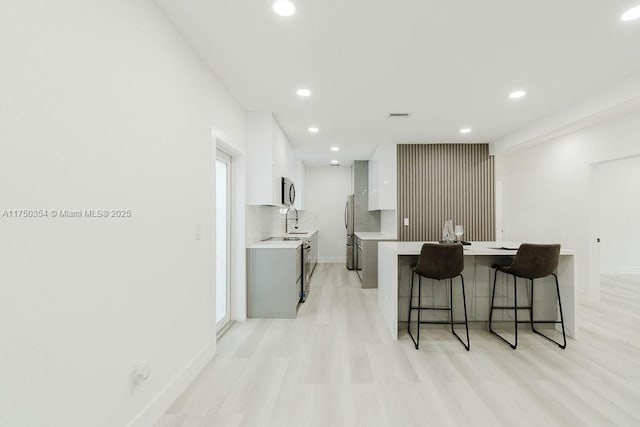 kitchen with modern cabinets, light countertops, light wood-style floors, white cabinetry, and a sink