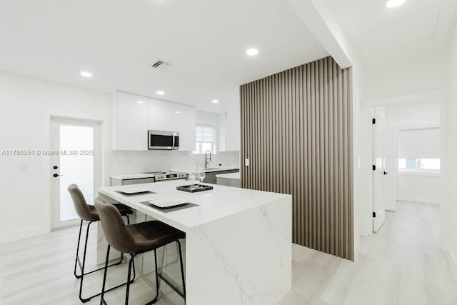 kitchen with modern cabinets, appliances with stainless steel finishes, white cabinetry, a kitchen island, and light stone countertops