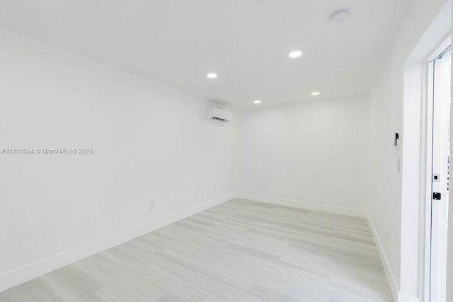 spare room featuring a wall unit AC, light wood-style floors, baseboards, and recessed lighting