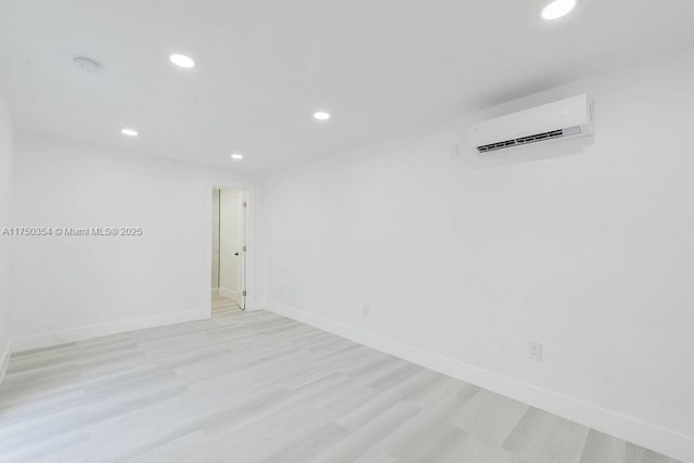 empty room with light wood finished floors, recessed lighting, baseboards, and a wall mounted AC