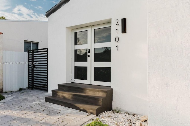 property entrance featuring french doors, a gate, and stucco siding