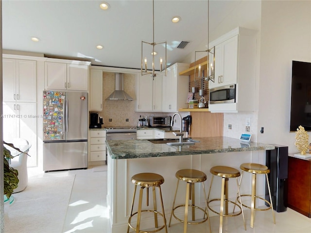 kitchen with stainless steel appliances, a sink, visible vents, wall chimney range hood, and dark stone countertops