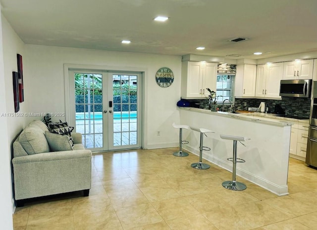 kitchen featuring french doors, stainless steel microwave, open floor plan, white cabinetry, and a peninsula