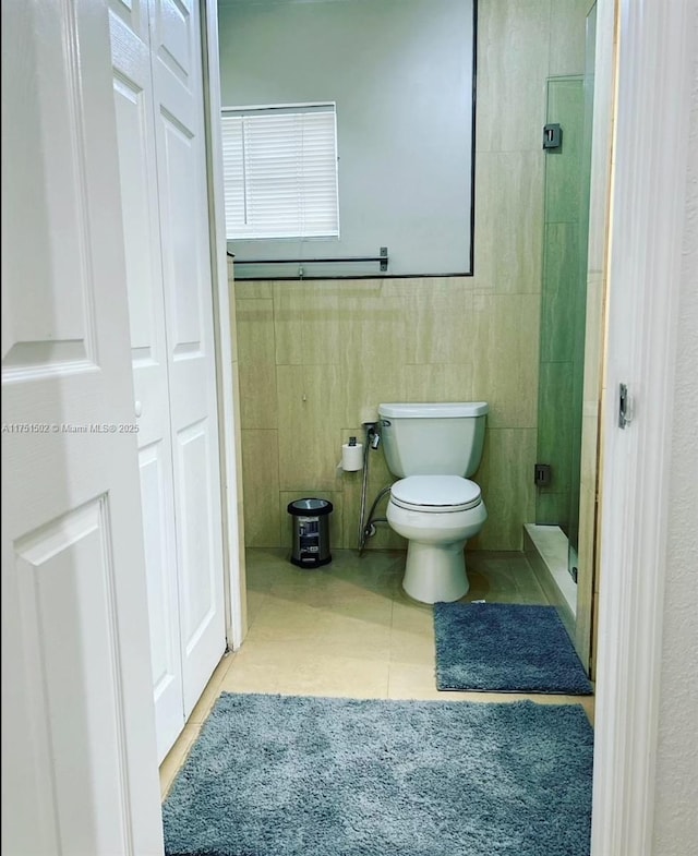 full bath featuring tile walls, a closet, toilet, a stall shower, and tile patterned flooring