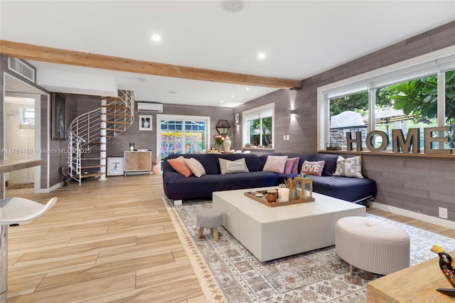 living area featuring visible vents, light wood-style floors, stairs, a wall mounted AC, and beamed ceiling