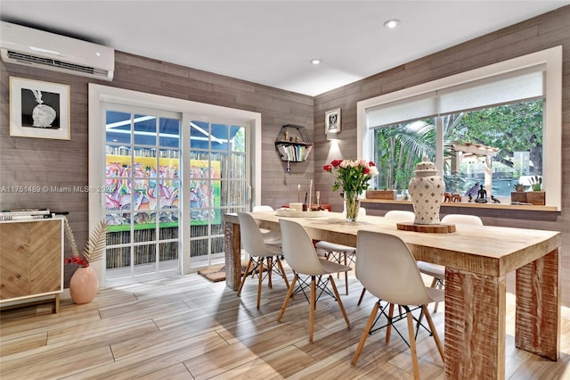 dining room featuring a wall mounted air conditioner, light wood-style flooring, and a healthy amount of sunlight