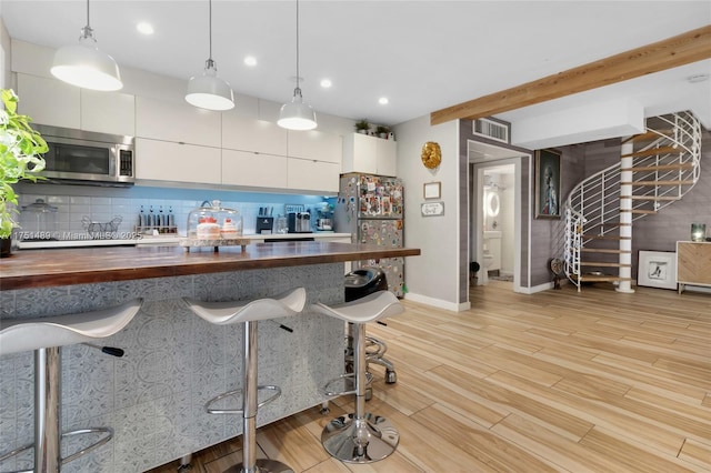 kitchen featuring pendant lighting, wooden counters, appliances with stainless steel finishes, white cabinetry, and modern cabinets