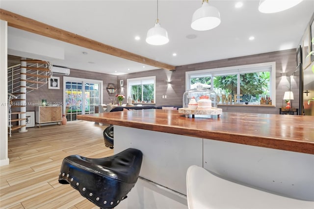 kitchen with butcher block counters, an AC wall unit, light wood-type flooring, pendant lighting, and beam ceiling