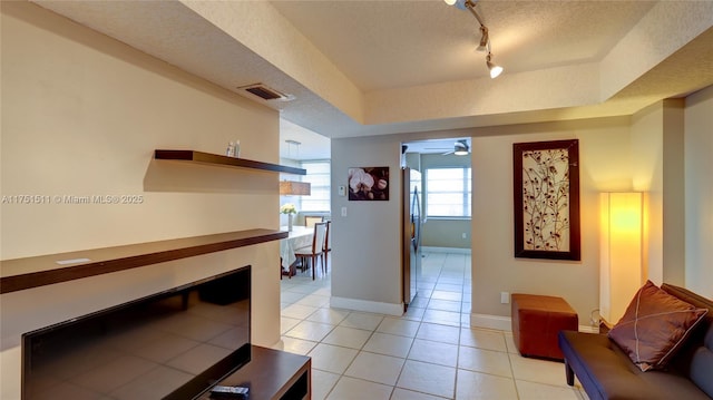 corridor with a textured ceiling, light tile patterned floors, visible vents, baseboards, and rail lighting