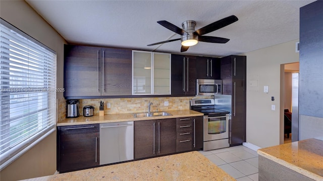 kitchen featuring light countertops, decorative backsplash, appliances with stainless steel finishes, glass insert cabinets, and a sink