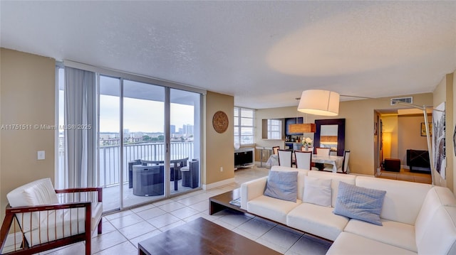 living area with floor to ceiling windows, visible vents, a water view, light tile patterned flooring, and a textured ceiling