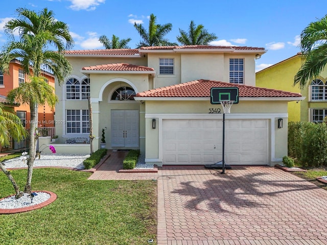 mediterranean / spanish house featuring a garage, a tiled roof, decorative driveway, stucco siding, and a front lawn