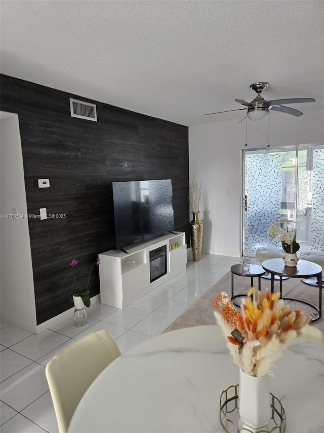 living room featuring light tile patterned floors, visible vents, an accent wall, a textured ceiling, and wood walls