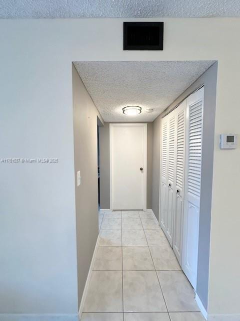 corridor with light tile patterned floors, baseboards, and a textured ceiling