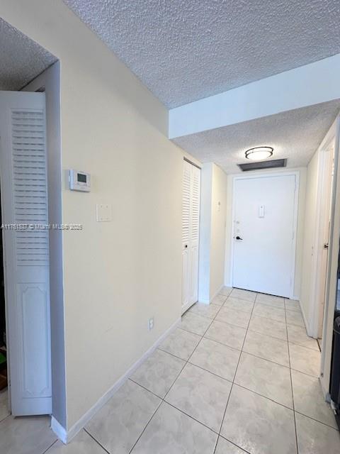 hallway featuring light tile patterned floors, baseboards, and a textured ceiling