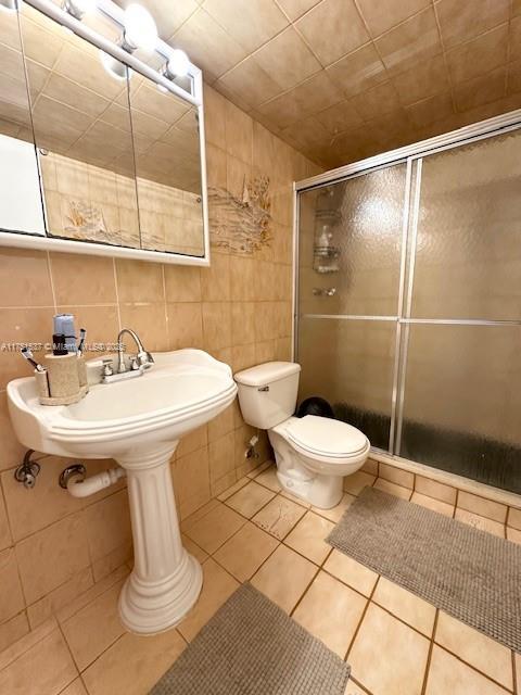 full bath with toilet, a stall shower, tile walls, and tile patterned floors