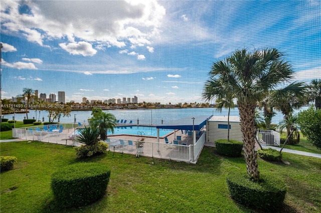 community pool featuring a lawn, a water view, fence, and a city view