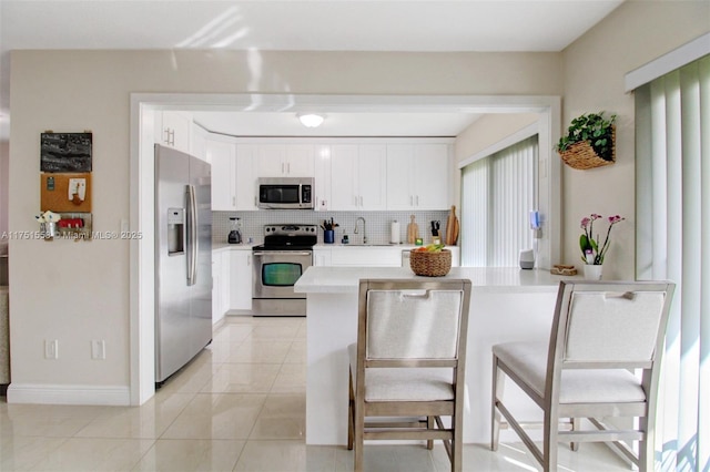 kitchen with tasteful backsplash, white cabinets, stainless steel appliances, light countertops, and a sink