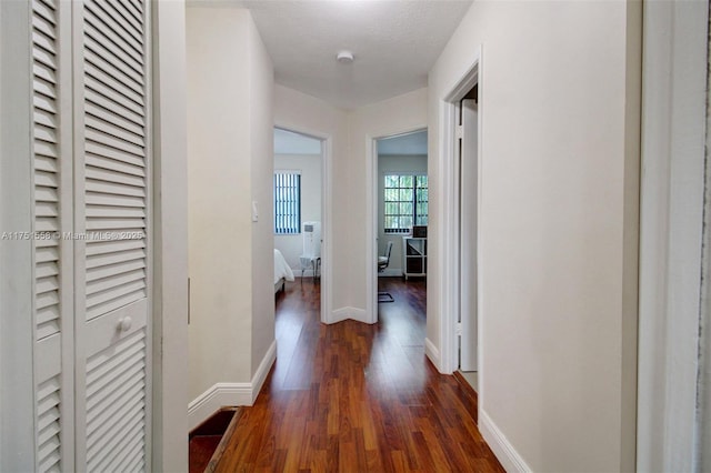 corridor featuring dark wood-type flooring and baseboards