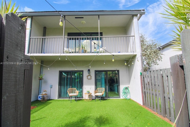 back of house with a yard, fence, a balcony, and stucco siding