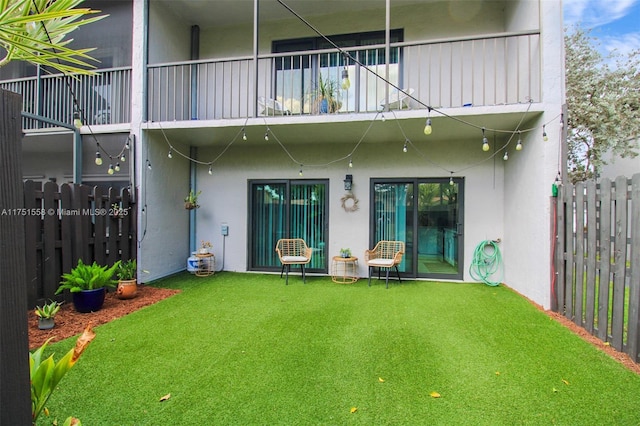 rear view of house featuring a lawn, fence, and stucco siding