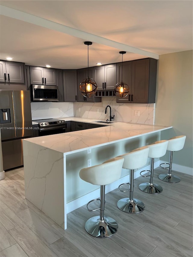 kitchen with a peninsula, stainless steel appliances, a kitchen bar, pendant lighting, and a sink