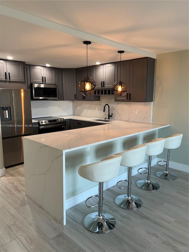 kitchen with a peninsula, appliances with stainless steel finishes, a sink, and decorative light fixtures