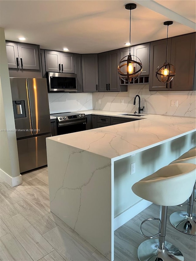 kitchen featuring a breakfast bar area, a peninsula, light stone countertops, stainless steel appliances, and pendant lighting