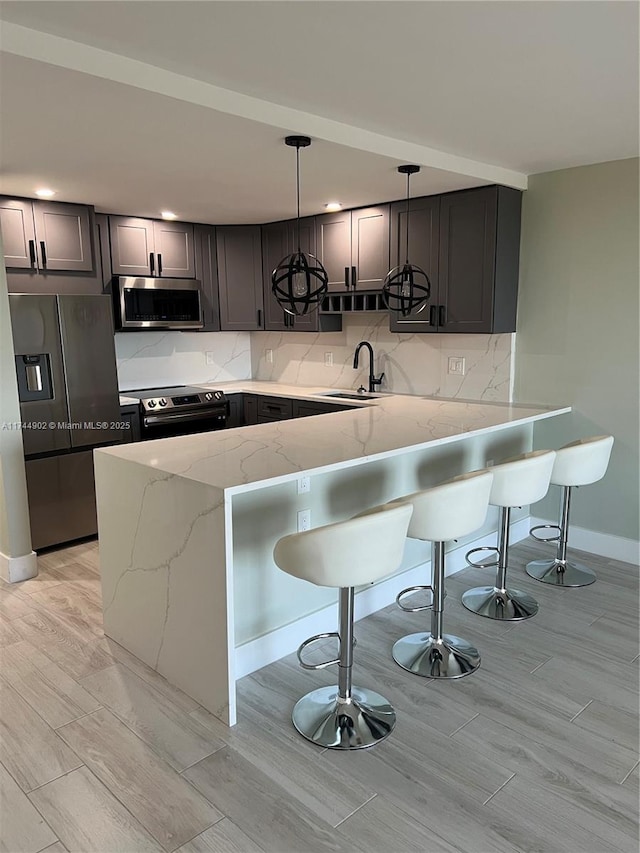 kitchen featuring a peninsula, light stone countertops, stainless steel appliances, pendant lighting, and a sink