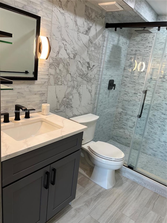 bathroom featuring tile walls, a shower stall, vanity, and toilet