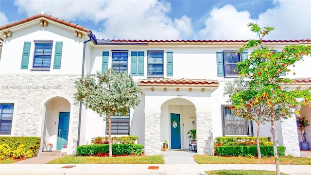 mediterranean / spanish house featuring stone siding, a tiled roof, and stucco siding