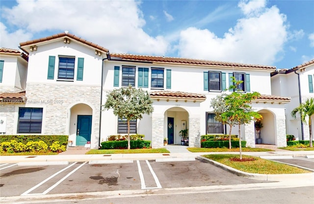 view of front of home with uncovered parking, stone siding, and stucco siding