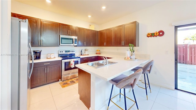 kitchen featuring a sink, stainless steel appliances, light countertops, and a kitchen breakfast bar