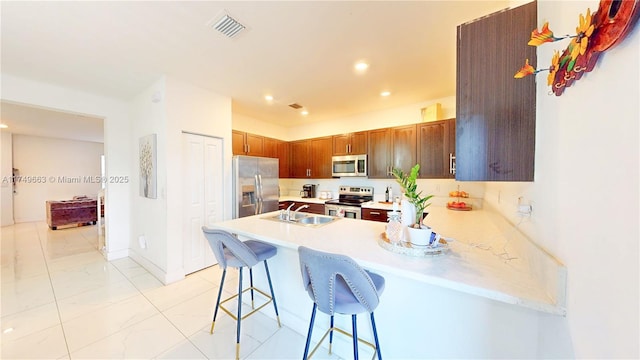 kitchen featuring light countertops, appliances with stainless steel finishes, a kitchen bar, and visible vents