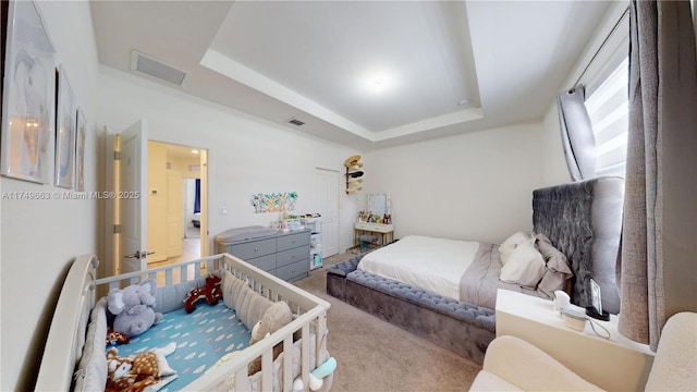 carpeted bedroom featuring a tray ceiling and visible vents