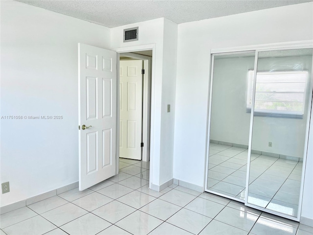 unfurnished bedroom with light tile patterned floors, baseboards, visible vents, a textured ceiling, and a closet