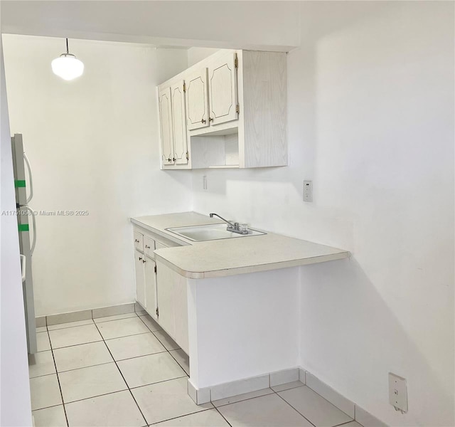 kitchen with light tile patterned floors, freestanding refrigerator, a peninsula, light countertops, and a sink