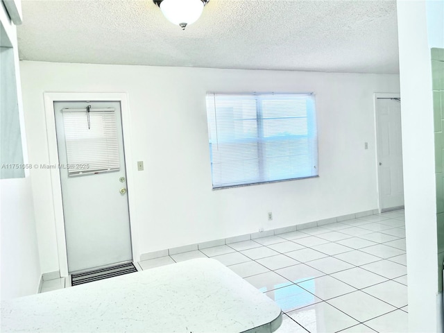 unfurnished room with baseboards, a textured ceiling, and light tile patterned flooring