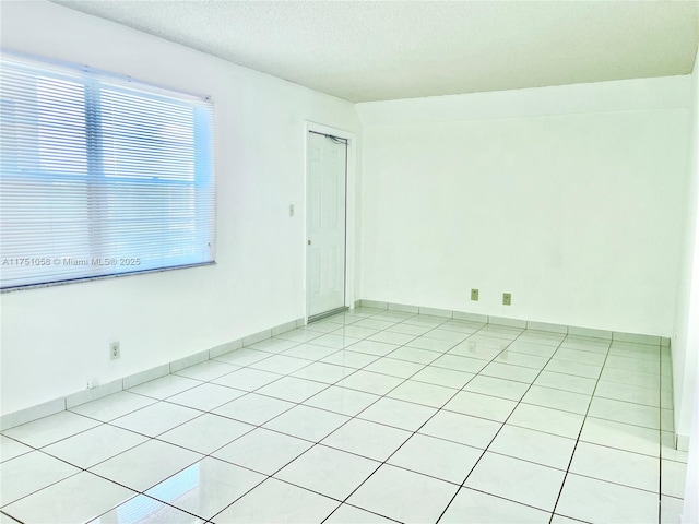 unfurnished room with baseboards, a textured ceiling, and light tile patterned flooring