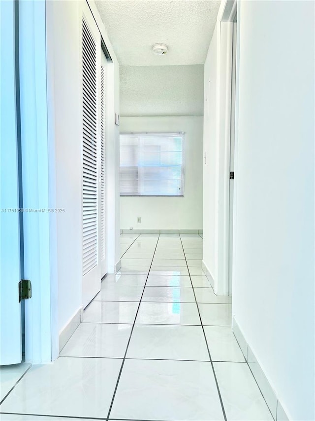 hallway with light tile patterned flooring, a textured ceiling, and baseboards