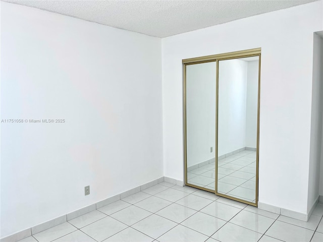 unfurnished bedroom with a closet, a textured ceiling, baseboards, and light tile patterned floors