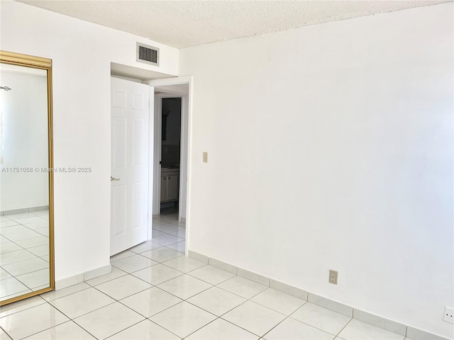 unfurnished room featuring light tile patterned floors, baseboards, visible vents, and a textured ceiling