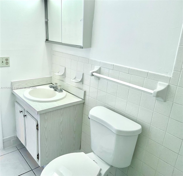 half bath with wainscoting, toilet, tile patterned flooring, vanity, and tile walls