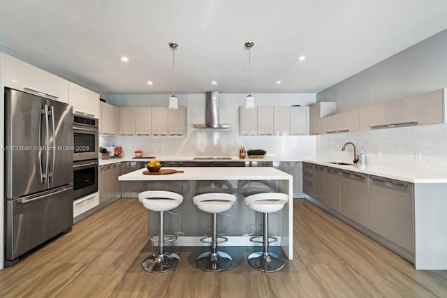 kitchen with wall chimney exhaust hood, appliances with stainless steel finishes, a center island, hanging light fixtures, and a sink